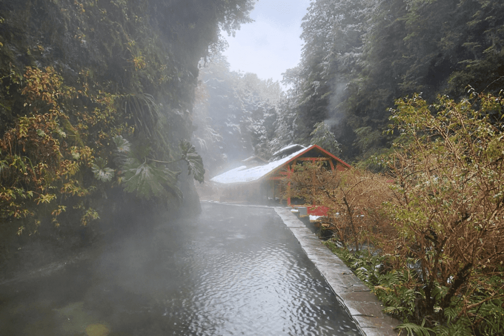 Arquitetura das Termas Geométricas integrada à natureza, com passarelas de madeira vermelhas e estruturas rústicas no Parque Nacional Villarrica, projetadas por Germán del Sol, Patagônia Chilena.