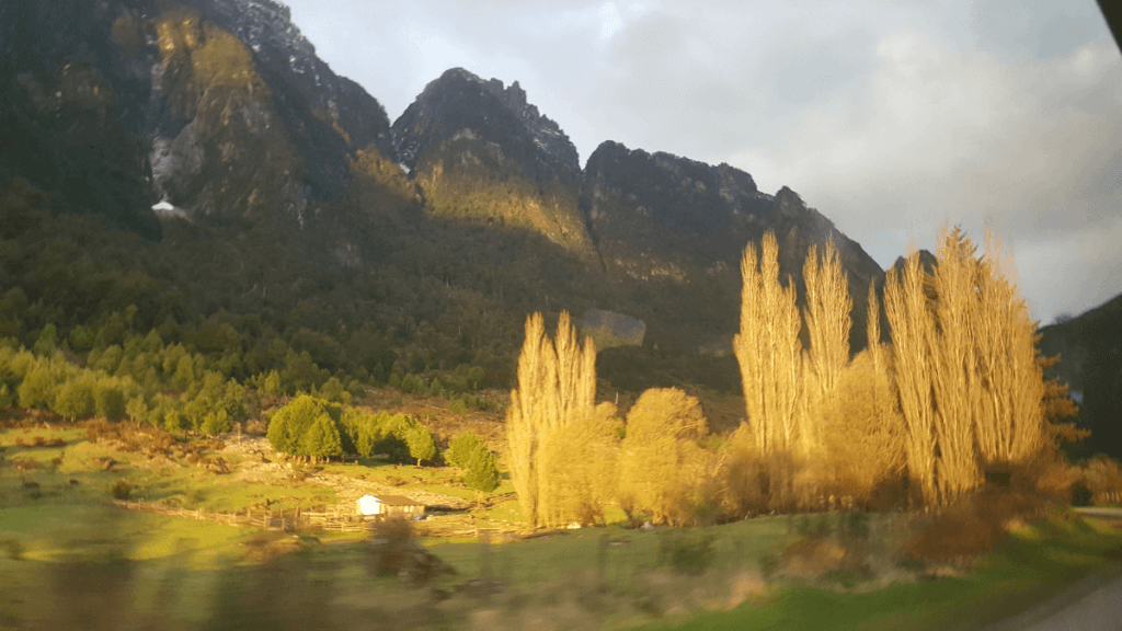 Paisagem bucólica na região de Aysén, com vegetação abundante e montanhas ao fundo, remetendo à atmosfera da Toscana.