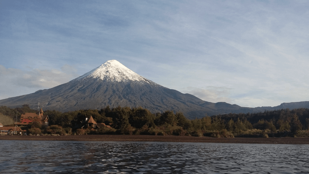 Vulcão Osorno com seu cume coberto de neve ao fundo, refletido nas águas calmas do lago na Patagônia Chilena.