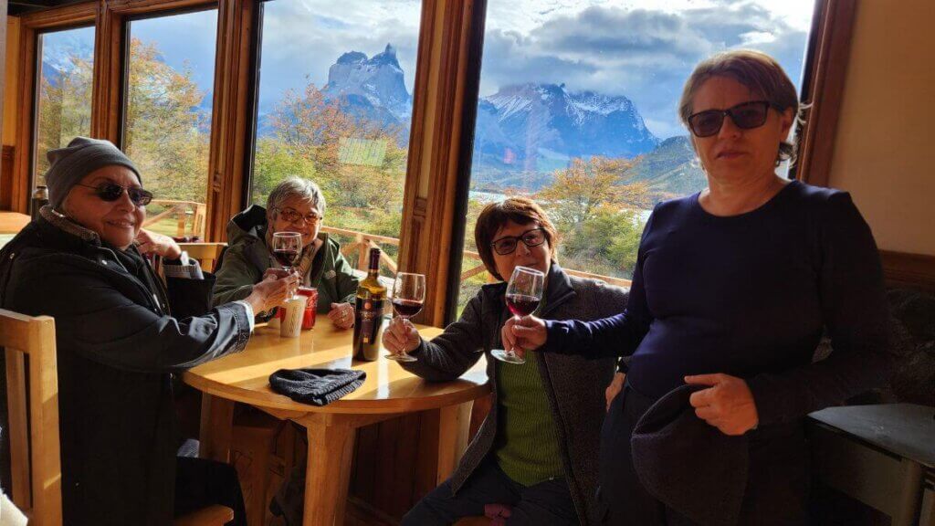 Interior de restaurante no Parque Nacional Torres del Paine, com taça de vinho em primeiro plano e os Cuernos del Paine ao fundo vistos pela janela