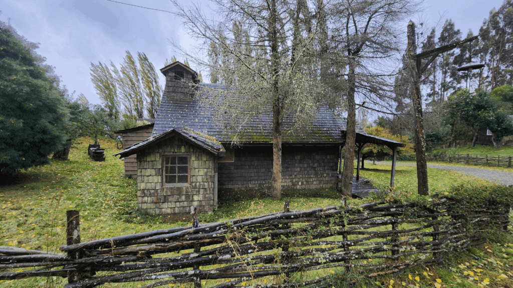 Casa tradicional chilota de madeira com tejuelas coloridas, cercada por denso bosque nativo de Chiloé, exemplificando a arquitetura vernacular da ilha em perfeita harmonia com a paisagem natural.