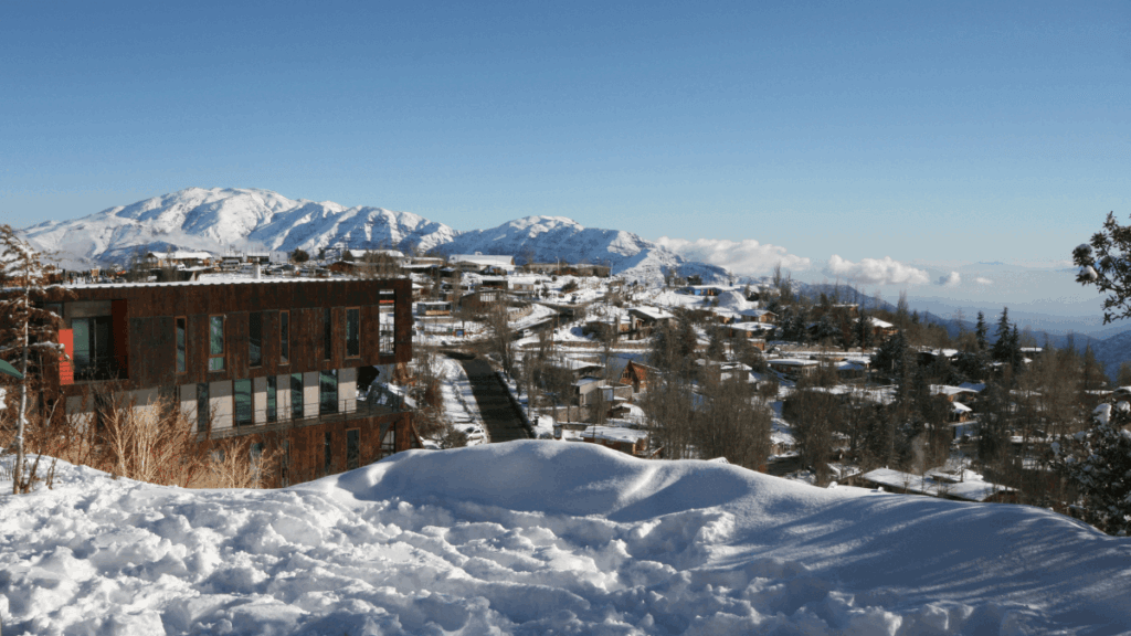 Vista panorâmica da cidade de Farellones coberta de neve, com casas de montanha e encostas nevadas no inverno chileno.