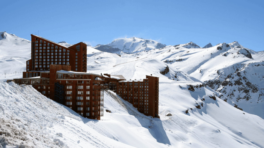 Foto de inverno em Valle Nevado com céu azul e o hotel ao fundo, cercado por neve nas montanhas da Cordilheira dos Andes.
