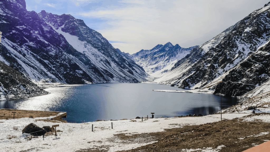 Lago de Portillo, com pouca neve ao redor e montanhas refletidas nas águas calmas do Lago del Inca.