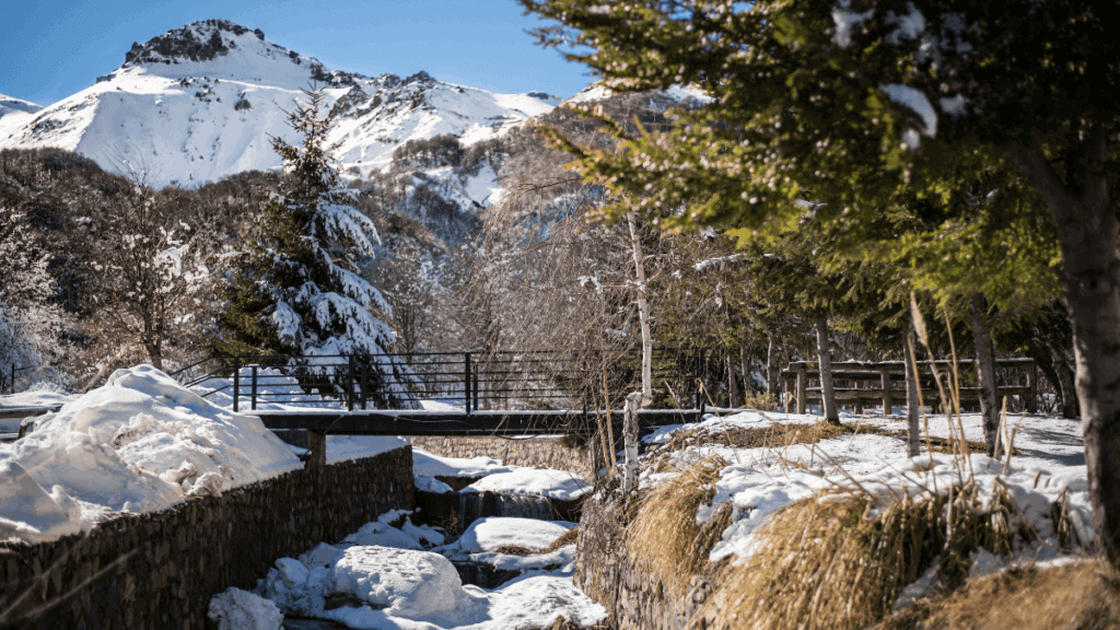 Rio parcialmente congelado em Nevados de Chillán, cercado por neve e vegetação andina durante o inverno no sul do Chile.