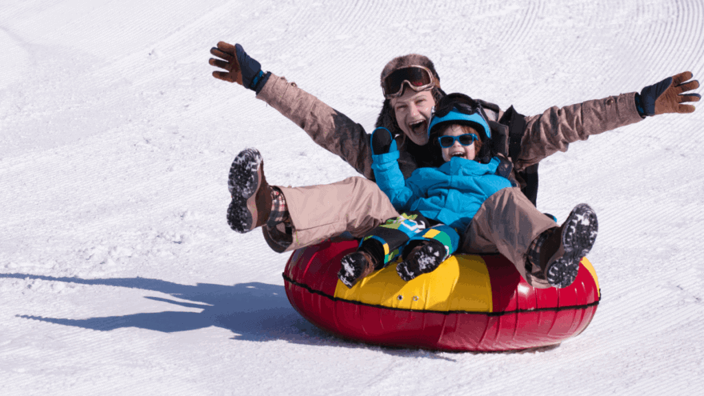 Mãe e filha escorregando na neve em uma boia inflável, sorrindo e se divertindo em estação de esqui na América do Sul.