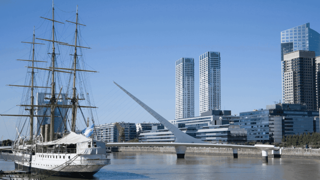 Puerto Madero em Buenos Aires, com prédios modernos, a Fragata Sarmiento e a Puente de la Mujer ao fundo, destaque para quem faz uma viagem a Buenos Aires.